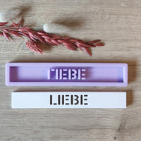 Easy-Sticks Silikonform 'Liebe' in lila und weiß, ideal für kreative Dekorationen und Geschenke, umgeben von Trockenblumen auf einem Holzuntergrund.