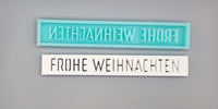 Zwei Silikonformen von Easy-Sticks mit dem Titel 'Easy-Sticks Silikonform - Frohe Weihnachten'. Die obere Form in Türkis zeigt den Schriftzug 'FROHE WEIHNACHTEN' und die untere Form in Weiß ist versehen mit der gleichen Inschrift in einer eleganten Schriftart.
