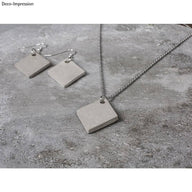 Trendige Schmuckanhänger aus Beton im Rautendesign von easy-sticks. Elegantes graues Set mit Ohrringen und Kettenanhänger präsentiert auf einem Betonuntergrund.