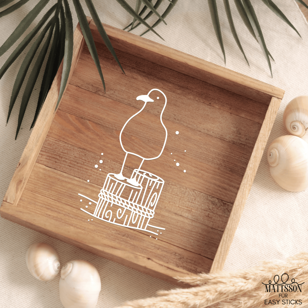 Holztablett mit stilisiertem Möwenmotiv, das auf einem Holzstamm steht, illustriert von easy-sticks, inspiriert von maritimen Plotter- und Laserdateien.