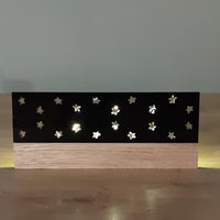Schwarze Acrylstern-Platte von Easy-Sticks, die an einer Holzunterlage angebracht ist. Die hochglänzende Oberfläche ist mit ausgefrästen Sternen dekoriert, die Licht durchscheinen lassen. Ideal für stimmungsvolle Dekorationen.
