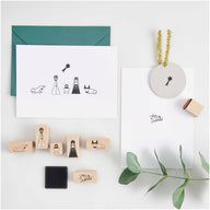 Das Stempelset "Krippe" von easy-sticks, bestehend aus 7 handgefertigten Stempeln, die die Weihnachtsgeschichte darstellen. Die Abbildung zeigt eine kreative Anordnung der Stempel, die Figuren wie Maria, Joseph, Ochse, Esel und einen Stern umfasst, zusammen mit Weihnachtskarten und einem Stempelkissen.