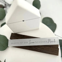 Elegante Holzunterlage mit der Inschrift 'GLÜCK IST DIE SUMME SCHÖNER MOMENTE', umgeben von einer weißen Box und Eukalyptusblättern, von easy-sticks, Teil der Rub on UV Sticker - randlos Winter A5 Kollektion.
