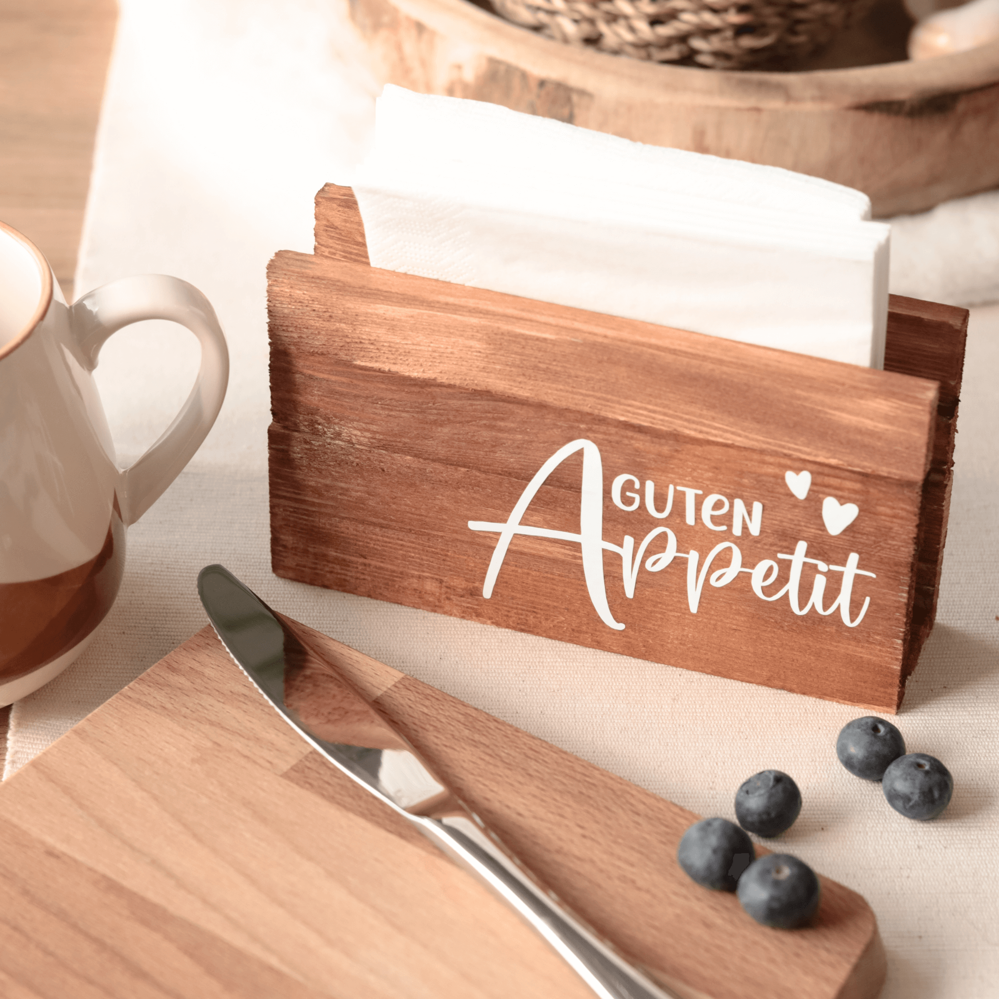 Stylischer Serviettenhalter "Guten Appetit" aus Holz, präsentiert mit Geschirr und einem Messer auf einem rustikalen Tisch, ideal für kreative Bastelprojekte mit der Plotterdatei von easy-sticks. Perfekt für einladende Essenssettings.