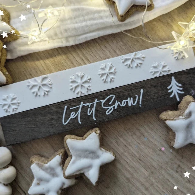 Schöne Winterdekoration mit der Easy-Sticks Silikonform - Schneeflocken, präsentiert auf einem Holztisch. Die Schneeflocken sind in einem kreativen Arrangement mit Keksen und Lichtern angeordnet.