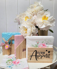 Charmante Präsentation des Serviettenhalters "Guten Appetit" von easy-sticks, umgeben von bunten Servietten und frischen Blumen, ideal für kreative Bastelideen und eine stilvolle Tischdekoration.