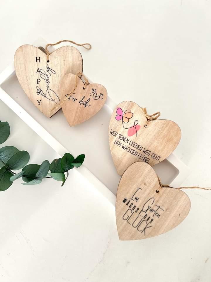 Vier herzförmige Holzanhänger mit verschiedenen Sprüchen, eine kreative DIY-Idee mit Easy-Sticks 'Rub on UV Sticker randlos Frühling'.