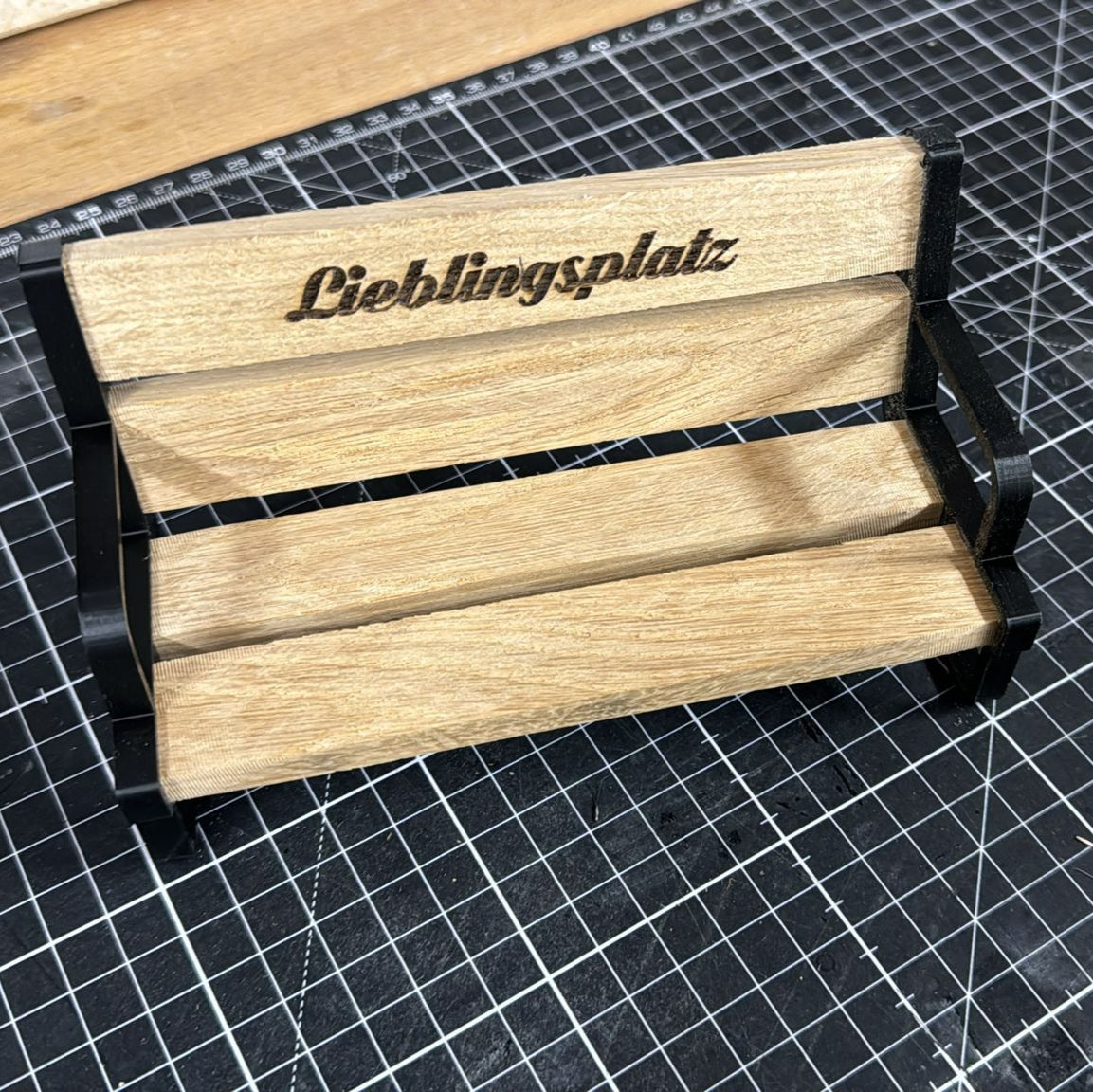 Dekorativer schwarzer Bankhalter von easy-sticks, gestaltet mit Holzoptik und dem Schriftzug 'Lieblingsplatz' für eine stilvolle Miniaturbank.