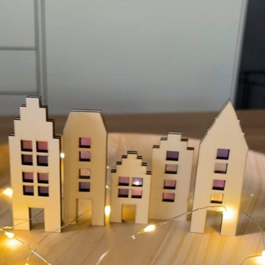 Dekorative Laser geschnittene Holzhäuser angeordnet mit Lichtern im Hintergrund, perfekt für individuelle Bastelprojekte. Häuser Plotterdatei zum Downloaden von easy-sticks.