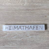 Transluzentes Acrylschild mit dem Schriftzug "HEIMATHAFEN" von Easy-Sticks, arrangiert auf einer Holzfläche.