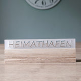 Acrylschild ohne Beleuchtung mit dem Schriftzug "HEIMATHAFEN" von Easy-Sticks, auf modernem Holzsockel platziert.
