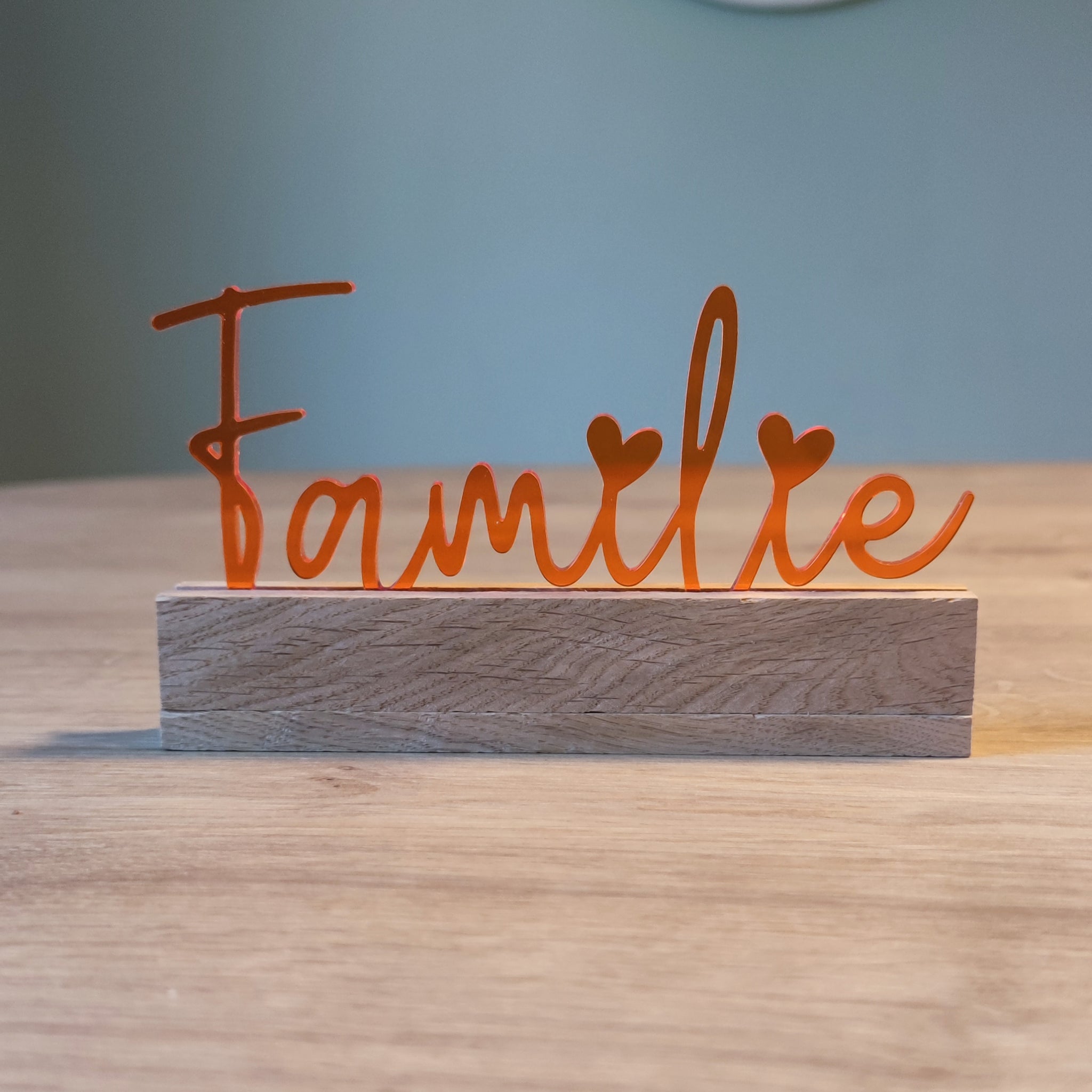 Acryl Aufsteller 'Familie' von Easy-Sticks in strahlendem Orange, dekorativ auf einem Holzsockel platziert und perfekt für das Wohnzimmer.