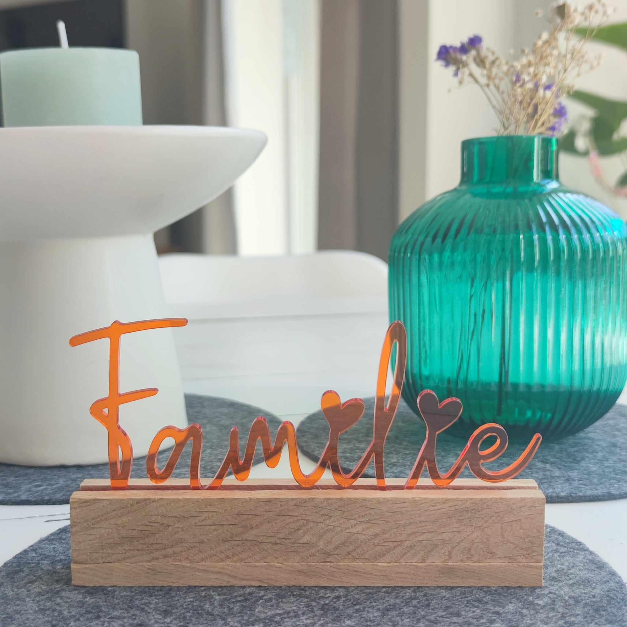 Eleganter acryl Aufsteller 'Familie' in orange von Easy-Sticks, dekorativ platziert auf einem Holzständer, umgeben von modernen Haushaltsgegenständen.
