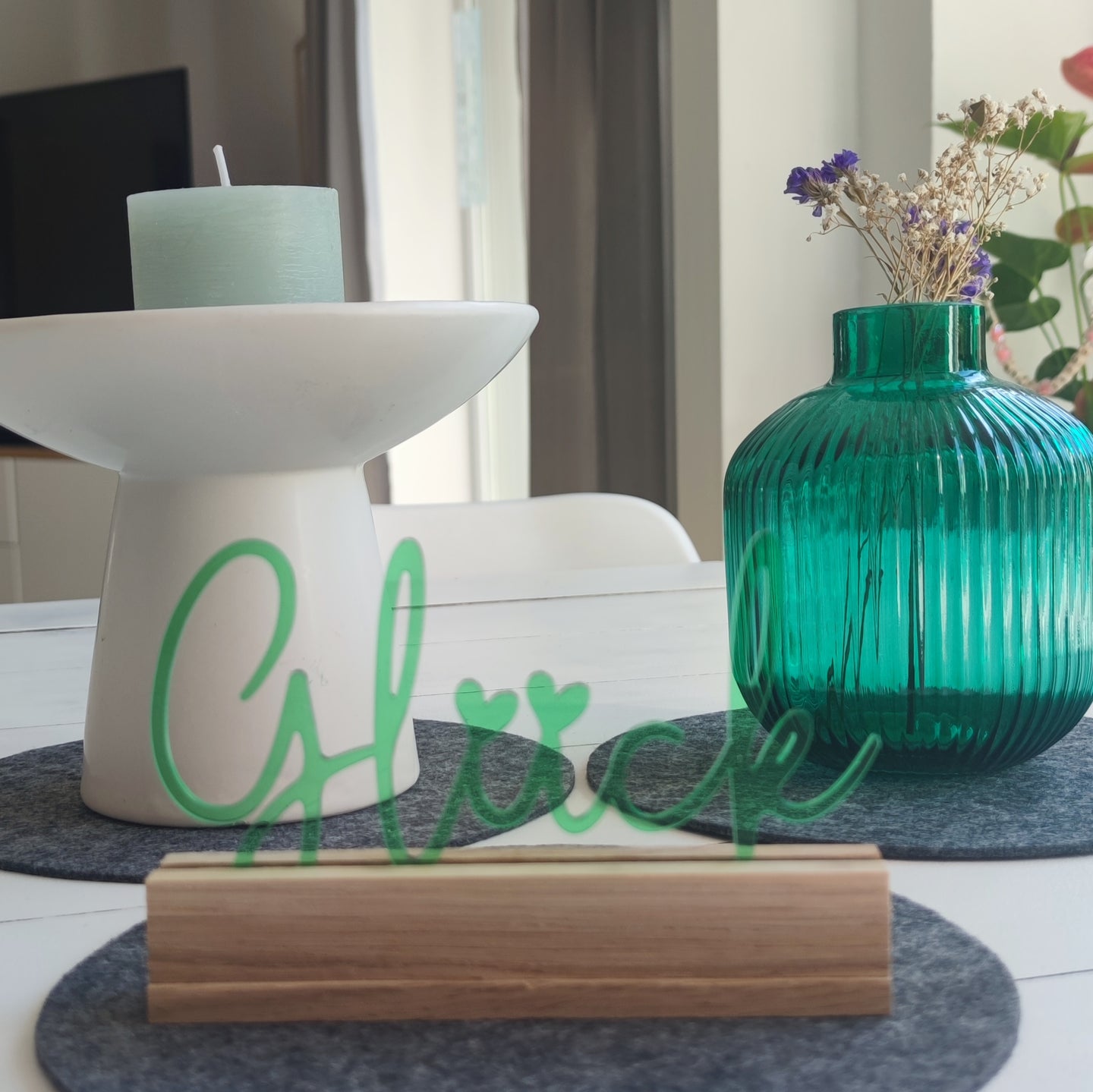 Easy-Sticks Acryl Aufsteller 'Glück' in sanftem Grün, präsentiert auf einem gedeckten Tisch neben einer blaugrünen Vase und einer Kerze, perfekte Deko für ein einladendes Ambiente.