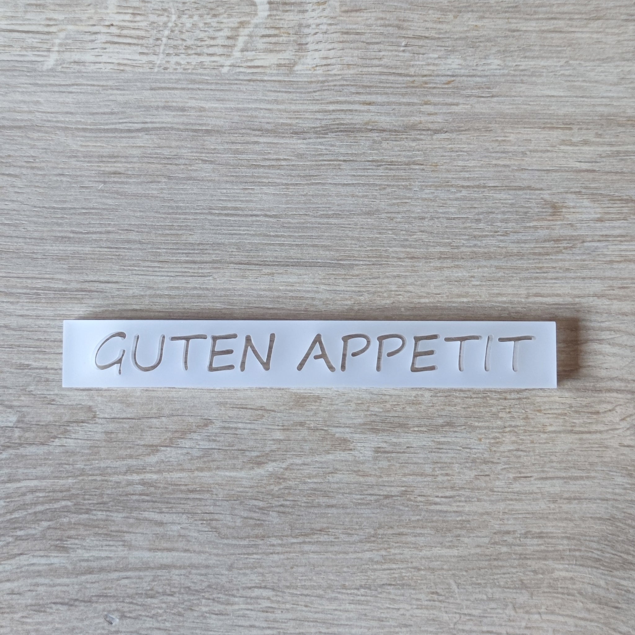 Minimalistisches Acrylschild von Easy-Sticks mit dem Text GUTEN APPETIT, stilvoll auf einem hellen Tisch platziert.