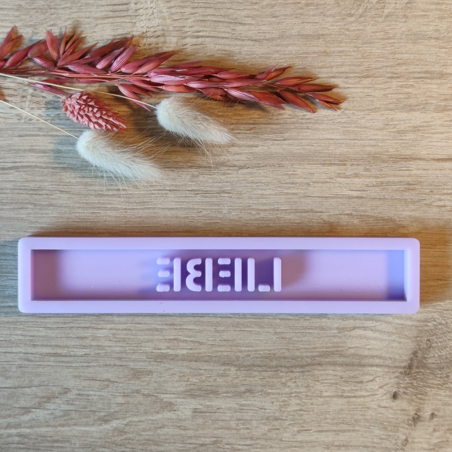Detaillierte Ansicht der lila Easy-Sticks Silikonform 'Liebe', dekoriert mit sanften Trockenblumen auf einem holzigen Tisch.