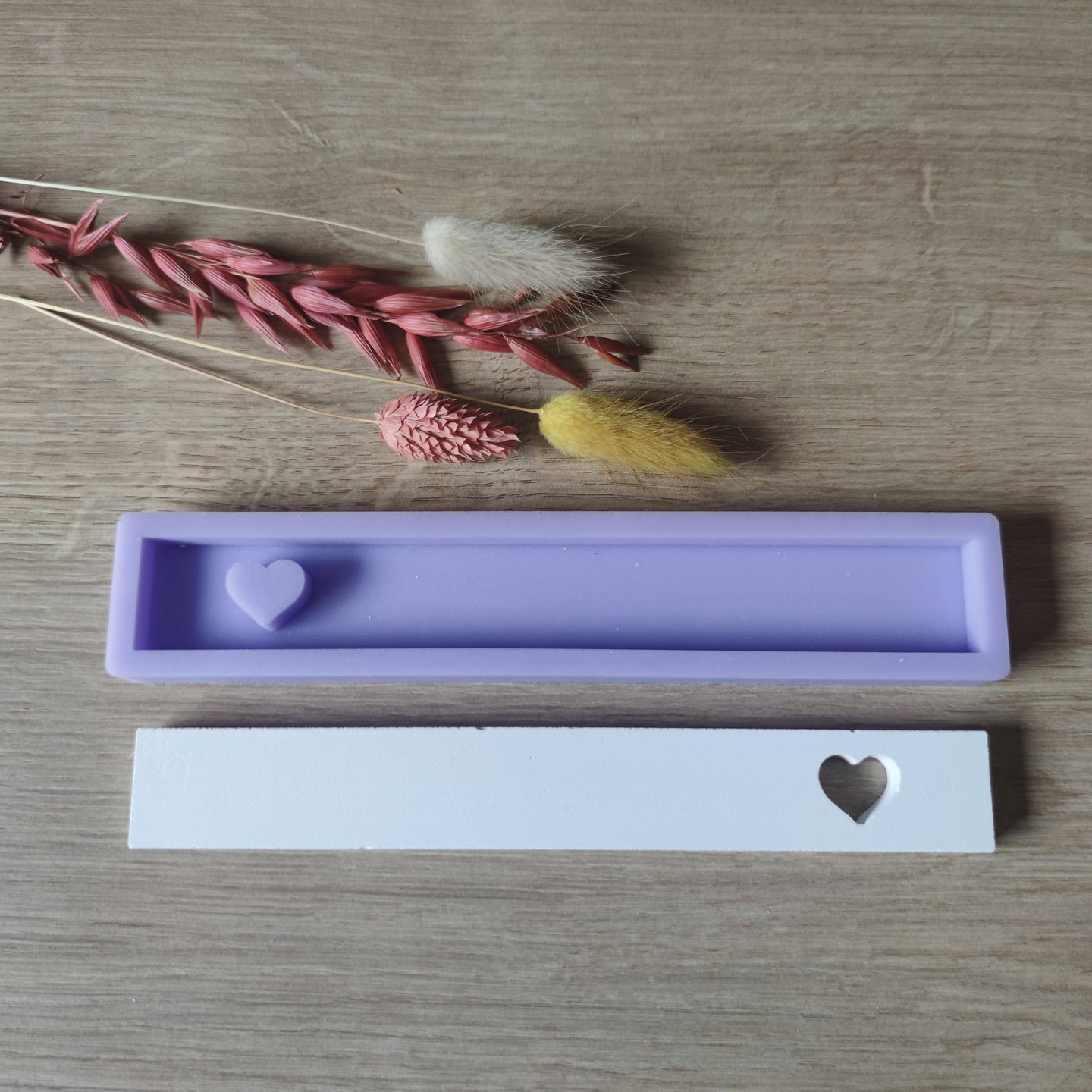 Easy-Sticks Silikonform mit Herz von Easy-Sticks, präsentiert auf einem Holzuntergrund, umgeben von Trockenblumen, ideal für kreative Bastelprojekte.