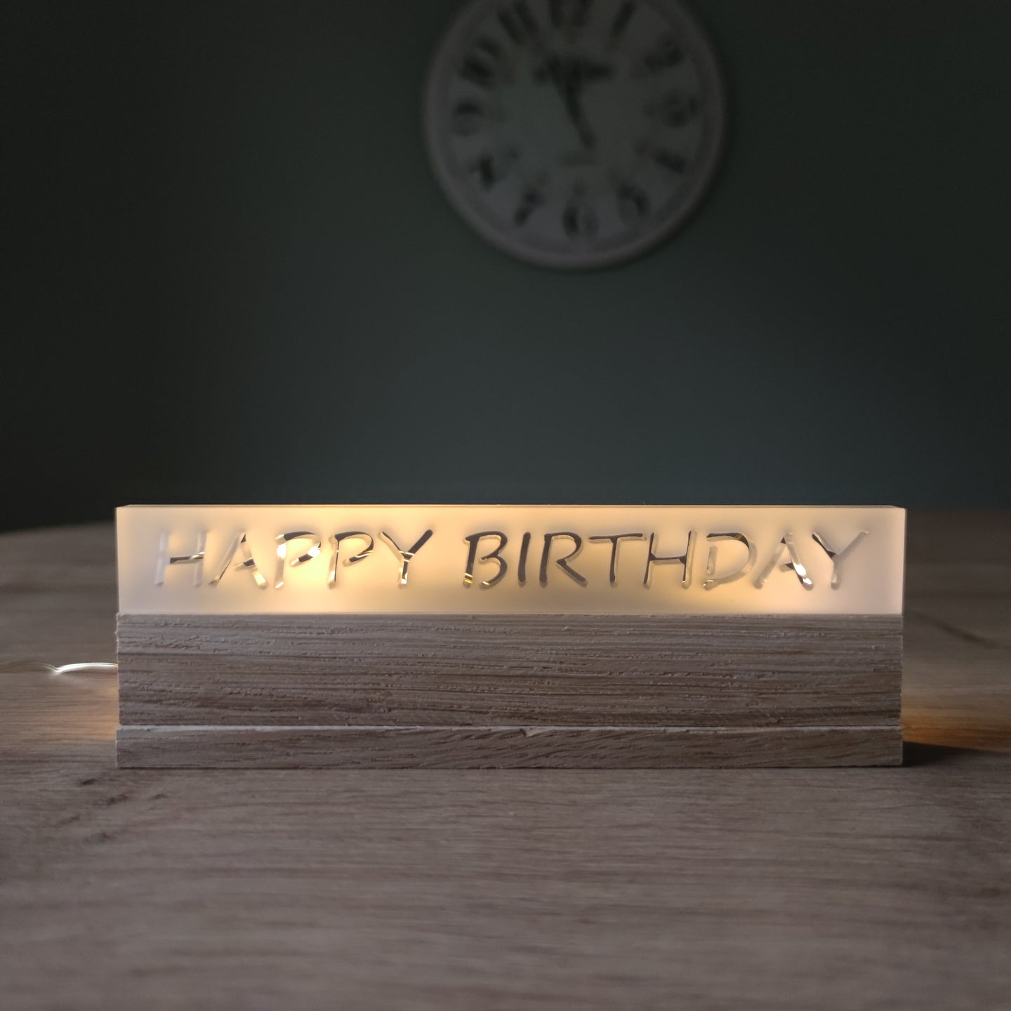Ein stilvoller Acryl-Schriftzug von Easy-Sticks mit der Aufschrift 'HAPPY BIRTHDAY', sanft beleuchtet und auf einem Holzsockel platziert, ideal für Geburtstagsfeiern.
