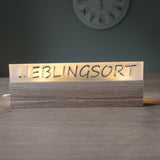 Beleuchtetes Acrylschild mit der Inschrift "LIEBLINGSORT" von Easy-Sticks, stilvoll auf einem Holzsockel angeordnet.