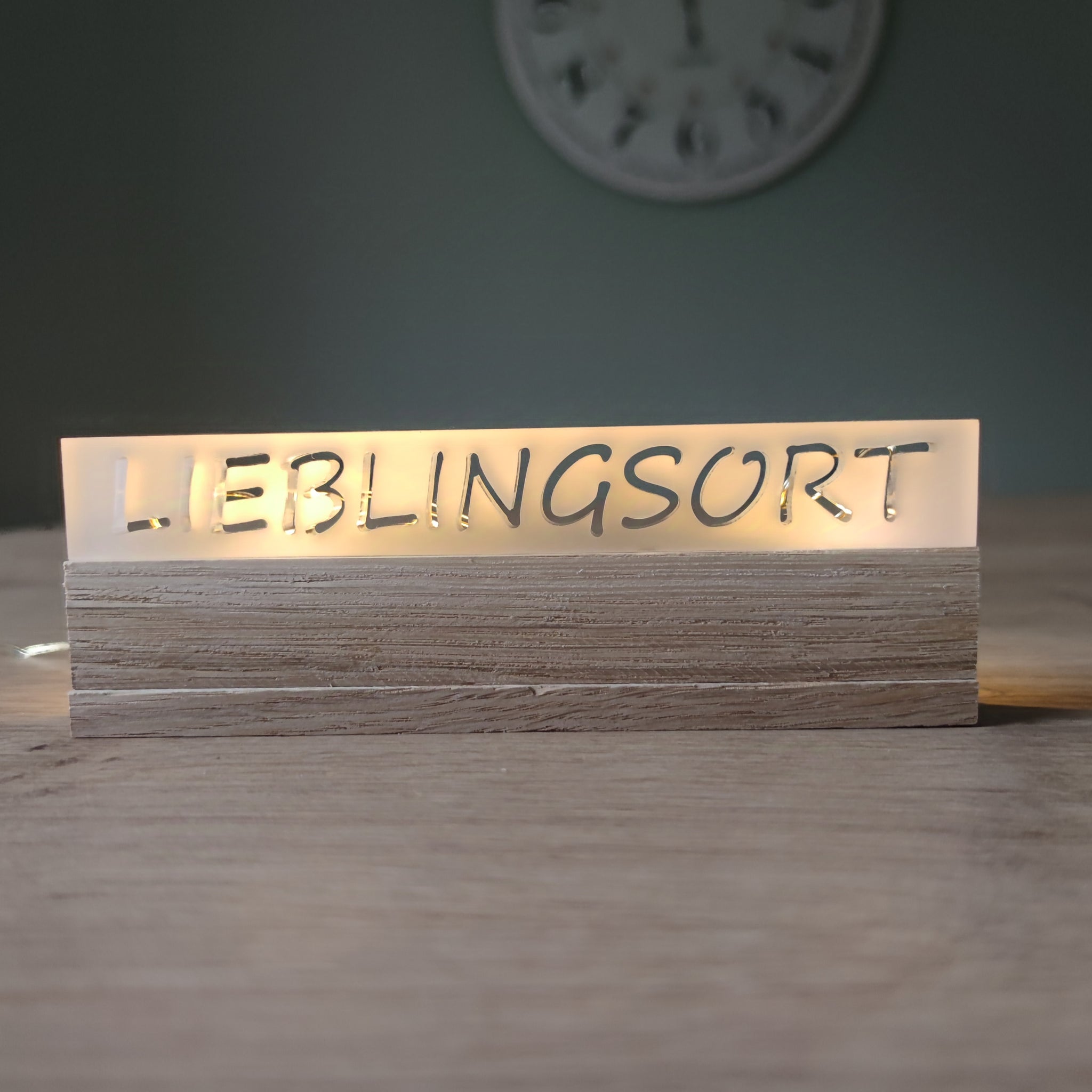 Beleuchtetes Acrylschild mit der Inschrift "LIEBLINGSORT" von Easy-Sticks, stilvoll auf einem Holzsockel angeordnet.