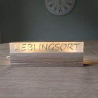 Beleuchteter Acrylschriftzug 'LIEBLINGSORT' auf einem Holzsockel, ideal für Dekoration. Easy-Sticks Acryl Satiniert.