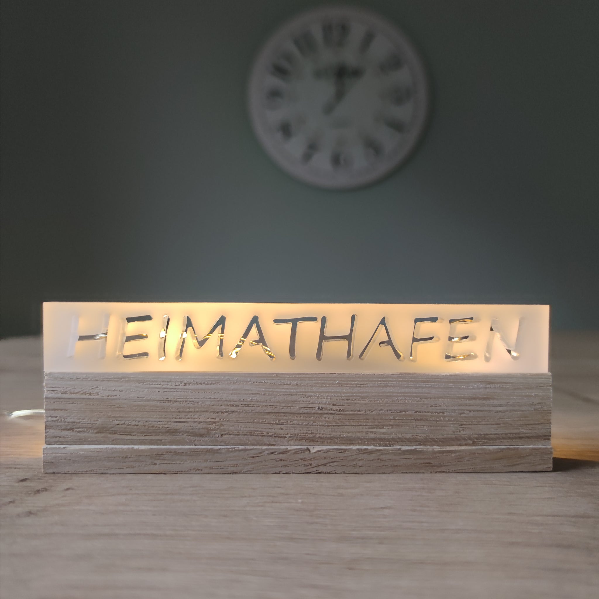 Beleuchtetes Acrylschild mit dem Schriftzug "HEIMATHAFEN" von Easy-Sticks, elegant präsentiert auf einem Holzsockel.