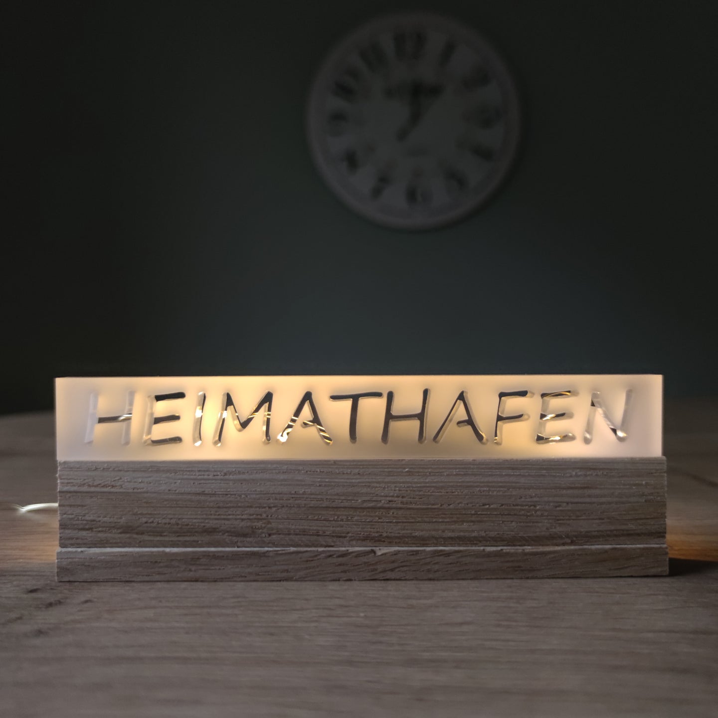 Beleuchtetes Acrylschild 'HEIMATHAFEN' von Easy-Sticks, elegant auf einem Tisch mit Holzoberfläche platziert, ideal als häusliche Dekoration oder Geschenk.