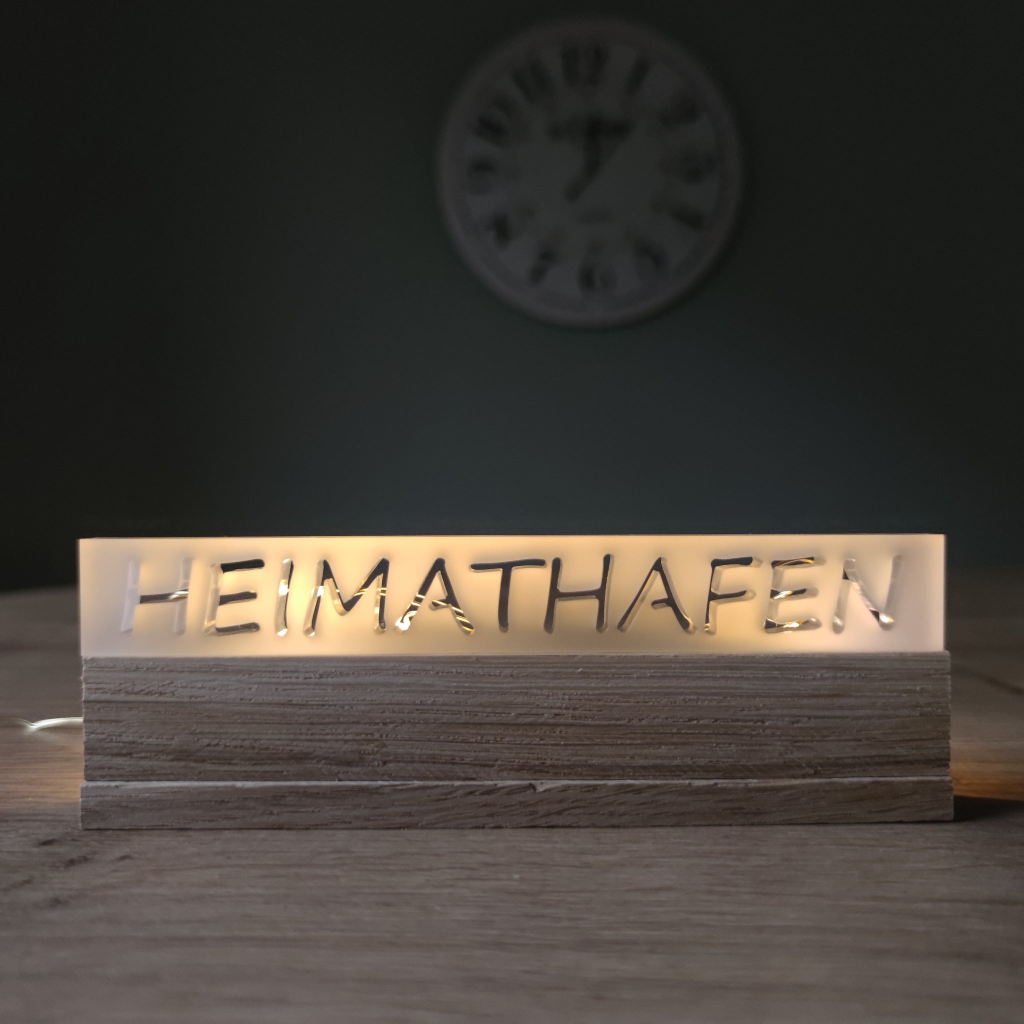 Beleuchtetes Acrylschild 'HEIMATHAFEN' von Easy-Sticks, elegant auf einem Tisch mit Holzoberfläche platziert, ideal als häusliche Dekoration oder Geschenk.