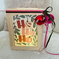handgefertigte HoHoHo Laterne, ideal für Weihnachtsdekoration, von easy-sticks. Begleitet von festlichen Glöckchen und farbiger Schleife, leuchtet die Laterne warm und gemütlich.