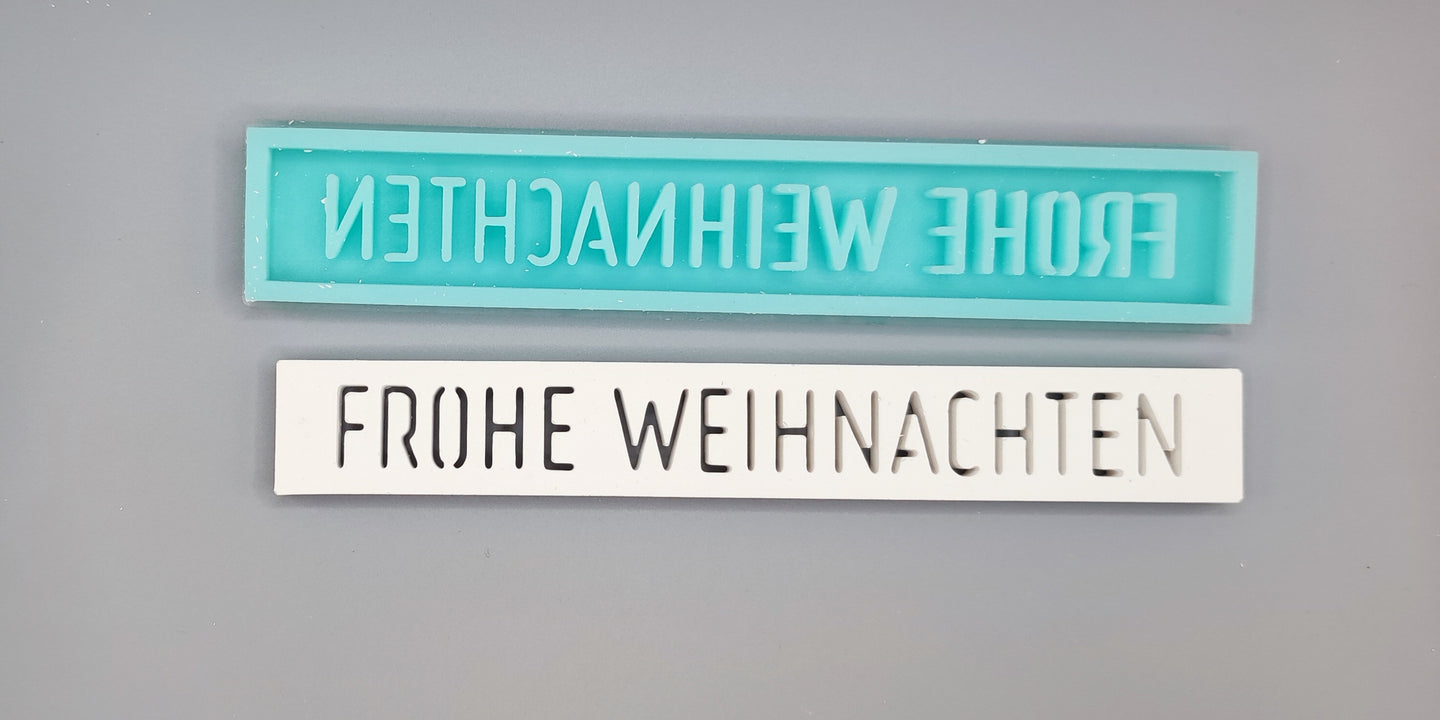 Zwei Silikonformen von Easy-Sticks mit dem Titel 'Easy-Sticks Silikonform - Frohe Weihnachten'. Die obere Form in Türkis zeigt den Schriftzug 'FROHE WEIHNACHTEN' und die untere Form in Weiß ist versehen mit der gleichen Inschrift in einer eleganten Schriftart.