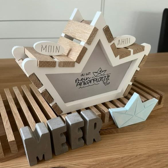 Dekorative Boot-Form von Easy-Sticks mit dem Titel 'Meer' und dem Spruch 'Du bist mein Ankerplatz'. Stilvolles Holzdesign auf einem Holzregal.