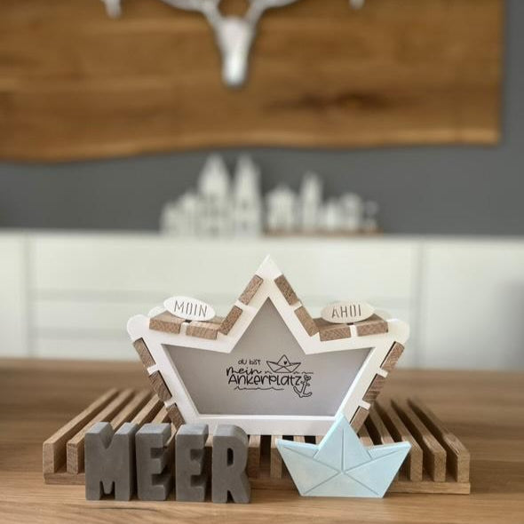 Detailaufnahme der Boot-Form von Easy-Sticks mit dem Titel 'Meer', einschließlich der Aufschrift 'MOIN' und 'AHOI', sowie einem kleinen Origami-Boot auf einem Holzregal.