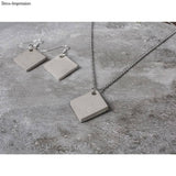 Trendige Schmuckanhänger aus Beton im Rautendesign von easy-sticks. Elegantes graues Set mit Ohrringen und Kettenanhänger präsentiert auf einem Betonuntergrund.