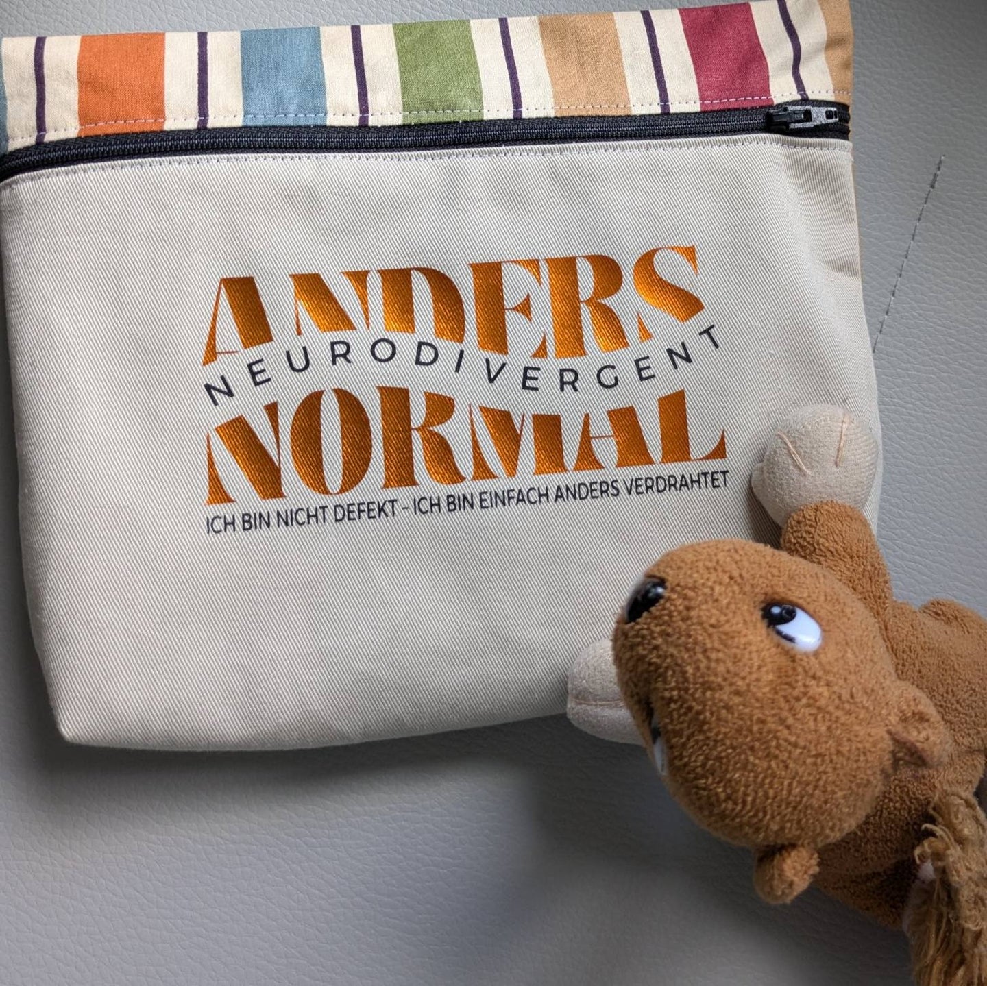 Ein einzigartiges Täschchen mit dem Aufdruck "Anders Normal Neurodivegent Ich bin nicht defekt - Ich bin einfach anders verdrahtet" von Easy-Sticks, begleitet von einem niedlichen Stofftier. Ideal für kreative Projekte und den täglichen Gebrauch.
