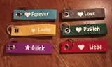 Bunte Anhänger mit verschiedenen Motiven und Sprüchen wie 'Forever', 'Läche' und 'Glück', ideal für kreative Projekte mit der Anhänger Teilchen Plotter- und Laserdatei von easy-sticks.