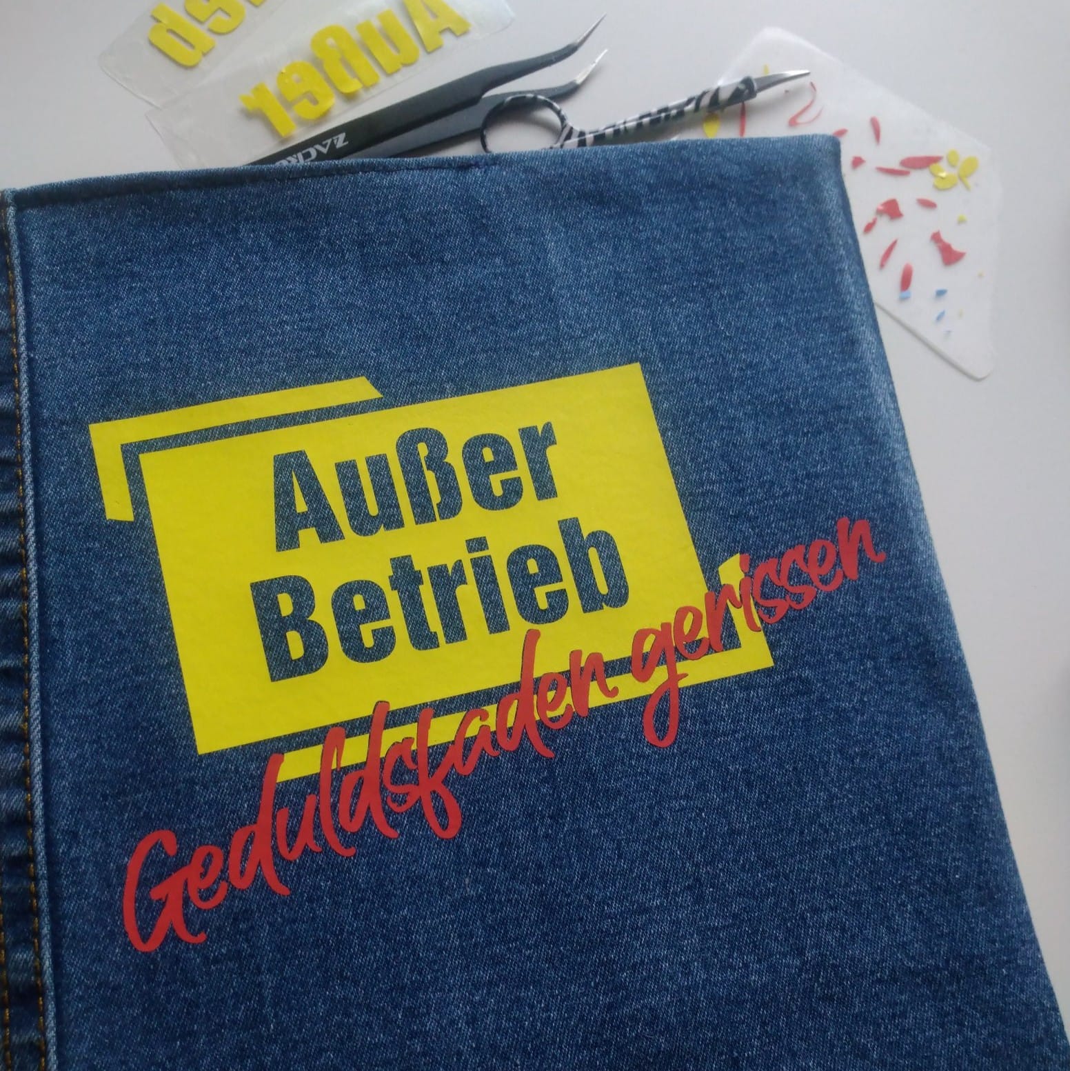 Anwendung der "Außer Betrieb - Geduldsfaden gerissen" Laserdatei von easy-sticks auf einer Jeans mit gelbem Schild und rotem Schriftzug.