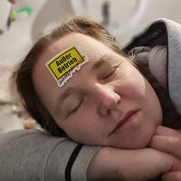 Frau ruht mit einem Sticker "Außer Betrieb - Geduldsfaden gerissen" von easy-sticks auf der Stirn, zeigt Entspannung und Humor.