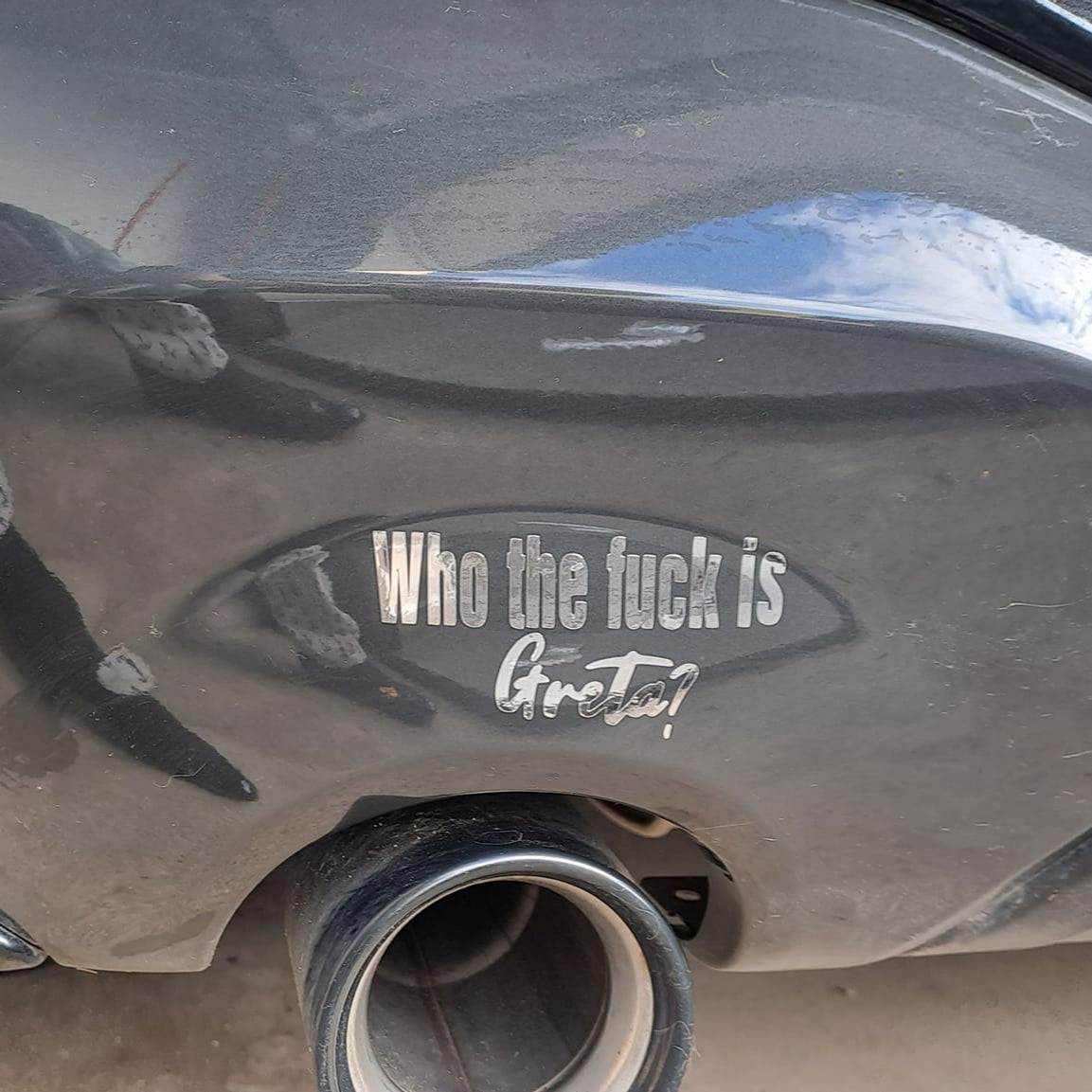 Nahaufnahme des Auspuffs eines Fahrzeugs mit dem Aufkleber "Who the fuck is Greta?" von easy-sticks, ideal für eine gewagte Gestaltung. Auto Sprüche Plotterdatei.