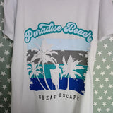 Ein stilvolles T-Shirt mit dem Aufdruck "Paradise Beach" und einem tropischen Design, das Palmen und eine Silhouette am Strand zeigt – ideal für kreative Projekte von Easy-Sticks mit der Plotterdatei "Beach".