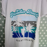 Ein stilvolles T-Shirt mit dem Aufdruck "Paradise Beach" und einem tropischen Design, das Palmen und eine Silhouette am Strand zeigt – ideal für kreative Projekte von Easy-Sticks mit der Plotterdatei "Beach".