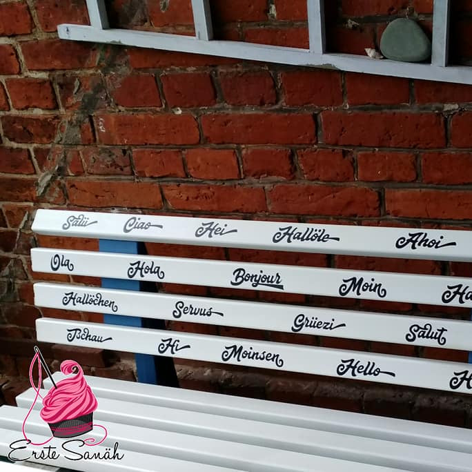 Eine kreative Sitzbank mit verschiedenen Sprachen der Begrüßung, darunter 'Moin', gestaltet mit der Plotterdatei 'Begrüßung und Abschied' von Easy-Sticks.