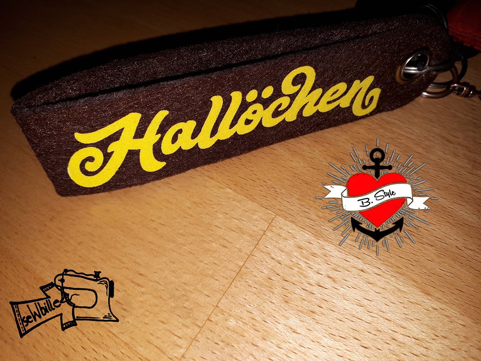 Ein braunes Schlüsselband mit dem eingestickten Wort 'Hallöchen' in gelber Schrift, inspiriert von der Plotterdatei 'Begrüßung und Abschied' von Easy-Sticks.