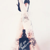 Feminines Bild mit tätowierten Beinen und einem Bier in der Hand, verziert mit einem lustigen Bierwärmer. Ausdrucksstark und kreativ, inspiriert von der Bier Sprüche Laserdatei von easy-sticks.
