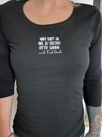 Dunkelhäutiges T-Shirt mit weißer Schrift "MAN SAGT JA VIEL ZU SELTEN BITTE DANK und Fick Dich" in der Mitte. Ton-in-Ton Näherin im Look, präsentiert von easy-sticks.