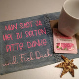 Denim-Stoff mit leuchtend pinker Schrift "MAN SAGT JA VIEL ZU SELTEN BITTE. DANKE. und Fick Dich" darauf liegend. Eine Tasse und ein Teebeutel sind daneben platziert. Entspannende DIY-Idee von easy-sticks.