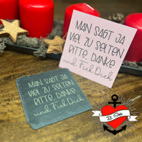 Schwarze Steinplatte mit goldener Schrift "MAN SAGT JA VIEL ZU SELTEN BITTE. DANKE. und Fick Dich" im Vordergrund. Im Hintergrund befinden sich rote Kerzen und Holzsterne. Kreative Gestaltungs-Idee von easy-sticks.