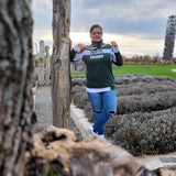 Eine Person in einem grünen Sweatshirt mit dem Spruch "bleib ANDERS" von easy-sticks, umgeben von Natur.