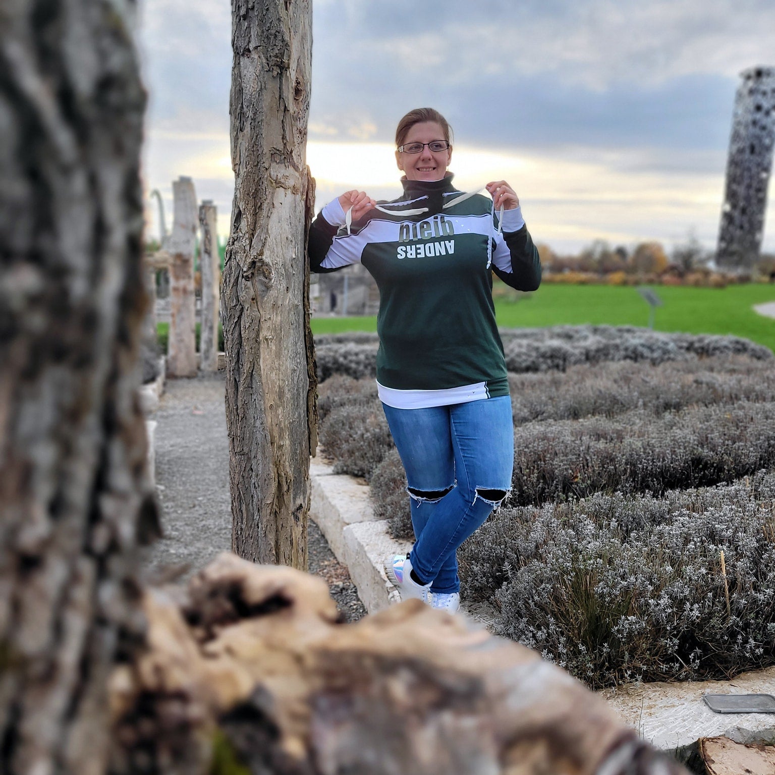Eine Person in einem grünen Sweatshirt mit dem Spruch "bleib ANDERS" von easy-sticks, umgeben von Natur.