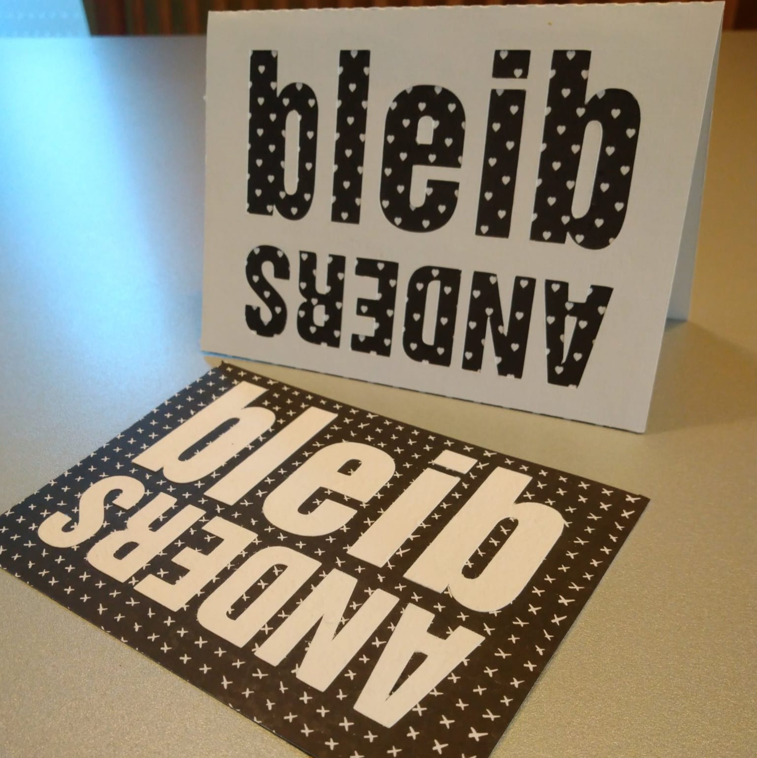 Zwei Karten mit dem designigen Spruch "bleib ANDERS" von easy-sticks, auf einem Tisch platziert.