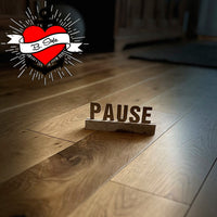 Buchstaben und Zahlen Aufsteller für Easy-Sticks Plotterdatei: Holzbuchstaben mit der Aufschrift 'PAUSE' auf einem gepflegten Holzfußboden, ideal für kreative Wohnideen.